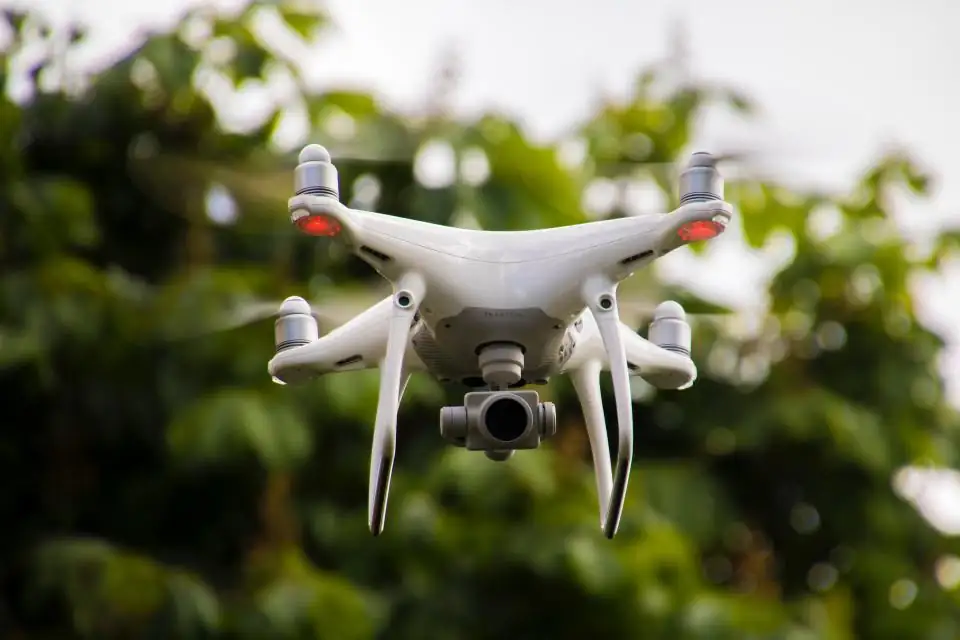 White camera drone flying above green trees