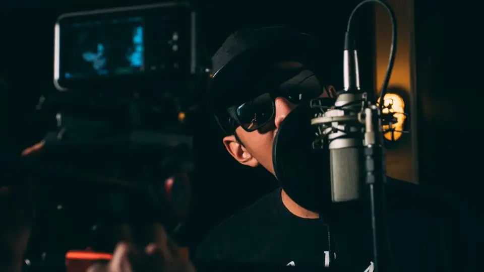 Person recording at a studio microphone with a camera behind